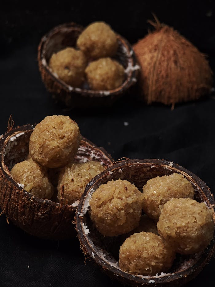 Mouth-watering coconut ladoo served in halved coconut shells on dark background.